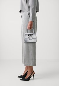 Metallic silver handbag with structured shape and top handle, paired with a black and white checkered suit and black high-heeled shoes.