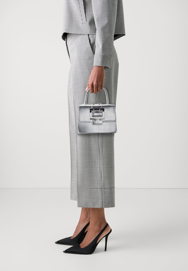 Metallic silver handbag with structured shape and top handle, paired with a black and white checkered suit and black high-heeled shoes.