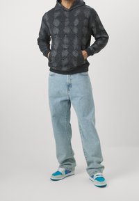 Felpa con cappuccio nera con un motivo a diamante testurizzato, abbinata a jeans dritti blu chiaro e sneaker multicolori.