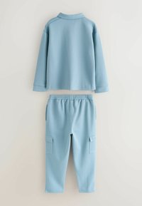 Helles blaues Zweiteiler-Outfit bestehend aus einem langärmeligen Polooberteil und passenden Cargo-Hosen mit Seitentaschen, gefertigt aus strukturiertem Stoff.