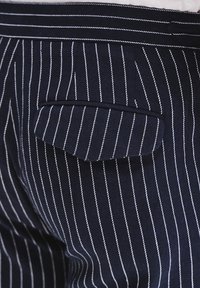 Granatowe spodnie w prążki o gładkiej fakturze, z kieszenią welt. Białe pasy rozmieszczone równomiernie, co tworzy klasyczny wzór.