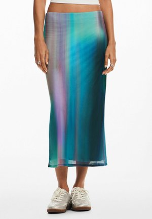 Vrouw die een lange, semi-transparante rok draagt met verticale strepen in een teal en paars verloop, gecombineerd met witte sneakers en ringen.