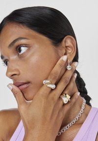 Anillos de plata y oro con diseños texturizados, pendientes en forma de aro con un detalle circular y un collar de cadena de plata gruesa.