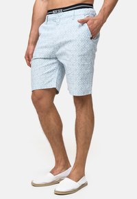 Shorts bleu clair à motifs avec un design géométrique, dotés d'une taille noire avec le logo "INDICODE", de poches latérales et d'une coupe décontractée.