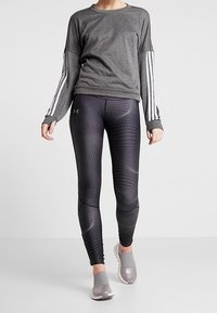 Camicia grigia a maniche lunghe con righe bianche sulle maniche, abbinata a leggins neri aderenti con un motivo a pois e un design testurizzato.