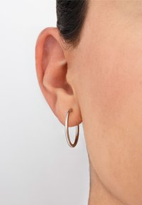 Pendiente de aro de plata reposando sobre una piel de tono claro. El pendiente presenta un diseño suave y redondeado, con una superficie reflectante.