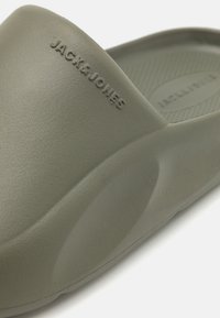 Sandale en caoutchouc verte à enfiler avec semelle texturée, portant le logo "JACK & JONES" en relief sur le côté et un design arrondi.