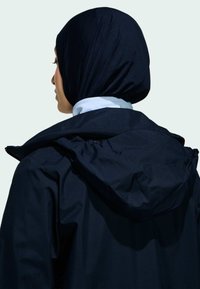 Námorná nepremokavá bunda s kapucňou, s hladkou textúrou a ľahkým dizajnom. Obsahuje vysoký golier a elastické detaily.