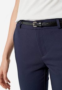 Granatowe, dopasowane spodnie o gładkiej fakturze z bocznymi kieszeniami, zestawione z wąskim, czarnym paskiem o fakturowanej powierzchni z srebrną klamrą.