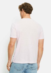 T-shirt rosa chiaro a maniche corte realizzato in un morbido tessuto testurizzato, con collo a giro e un piccolo dettaglio con etichetta sul lato.