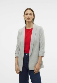 Blazer gris clair avec revers, manches retroussées et texture douce, associé à un haut rouge texturé et un jean taille haute bleu marine.