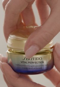 Shiseido Vital Perfection ögonkräm i en liten glasburk med ett guldlock och en graduerad blå bas. Etiketten visar produktinformation i svart.