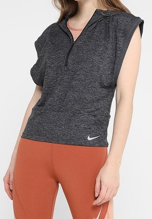 Kvinde iført en ærmeløs mørkegrå lynlåstop og højtaljede leggings i brændt orange med Nike-logoer på begge beklædningsdele.