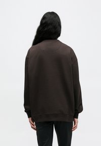 Καφέ φαρδιά μπλούζα με στρογγυλή λαιμόκοψη και χαμηλωμένους ώμους. Μανσέτες και τελείωμα με ριμπ ύφανση, απαλή υφή και μινιμαλιστικό σχέδιο.