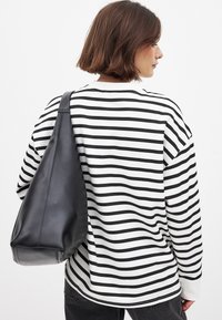 Črno-bela črtasta dolga majica je kombinirana z gladko črno torbo s širokim naramnicami in mehko teksturo.