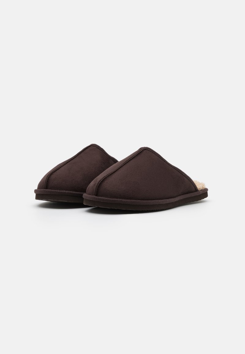 Zapatillas de tela marrón con un forro suave y peludo, forma redondeada y detalles cosidos. Diseñadas para la comodidad en interiores, con una suela plana.