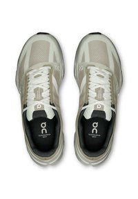 Beige und weiße Lauf Schuhe mit Mesh-Obermaterial, flachen Schnürsenkeln, gepolstertem Kragen und kontrastierender schwarzer Innensohle. Mit Logo an der Seite.