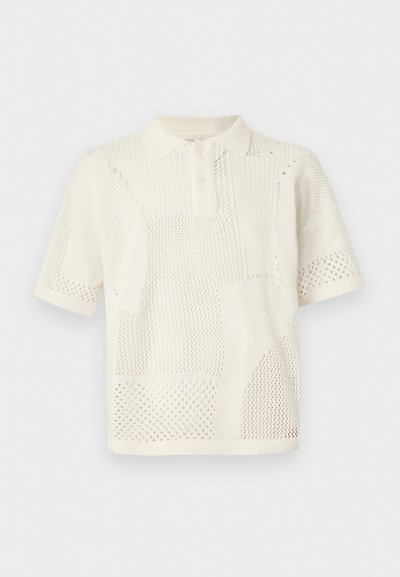 Πλεκτό πόλο με κοντά μανίκια σε κρεμ απόχρωση με ποικίλα ανοιχτά σχέδια πλεξίματος και κουμπωτό γιακά σε ουδέτερο φόντο.