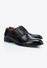 Les chaussures habillées en cuir noir présentent une finition lisse, un bout rond et un laçage à cinq œillets. Des accents brodés discrets le long des côtés et un talon bas.