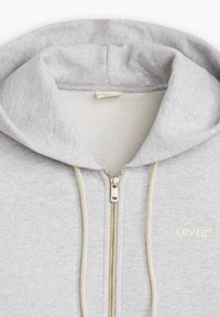 Felpa grigia con zip realizzata in morbida miscela di cotone. Presenta un cappuccio foderato, coulisse color crema e un logo discreto sul petto. Chiusura con cerniera argentata.