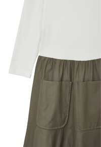 Maglietta a maniche lunghe in cotone bianco con gonna verde oliva a trapezio, dotata di vita elastica e due grandi tasche frontali.
