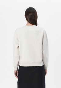 Lichtbeige sweatshirt met een ronde hals, ribgebreide manchetten en zoom. De stof lijkt zacht met een licht gestructureerde afwerking. Draag het met een zwarte rok.