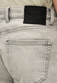 Γκρι τζιν από denim με υφασμάτινη ζώνη στη μέση και μαύρο δερμάτινο σημείο με την ένδειξη "MICHAEL KORS." Διαθέτει δύο πίσω τσέπες και ραφές με λεπτομέρειες.