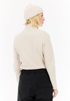 Beige fleece pullover met een hoge kraag, zachte textuur, en een geribde crèmekleurige beanie. Zwarte elastische tailleband met een patchzakje op de broek.