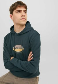 Sudadera de color verde oscuro con un logo frontal que presenta "Jack & Jones". Tiene cordones, un corte relajado y puños y dobladillo acanalados.