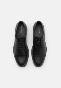 Chaussures habillées en cuir noir avec une finition lisse, bout arrondi et système de laçage. Présente des perforations minimales sur le dessus.