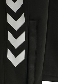 Black fabric with a vertical row of five white downward-pointing chevrons next to a vertical stitched seam or pocket edge.