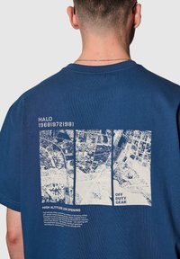 Marinblå bomulls t-shirt med en vit grafik av flygbilder på baksidan, tillsammans med texten "HÖG HÖJD LÅG ÖPPNING."
