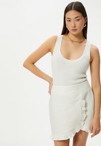 Débardeur blanc côtelé associé à une mini-jupe blanche texturée avec un ourlet en biais. Design simple avec une silhouette ajustée.