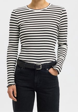 Personne portant un haut à manches longues rayé horizontal noir et blanc rentré dans un jean noir taille haute avec une ceinture noire.