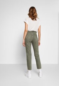 Pantalones de mezclilla verde oliva de talle alto con un corte entallado, que cuentan con grandes bolsillos traseros y un lazo para cinturón, combinados con una camiseta de rayas.