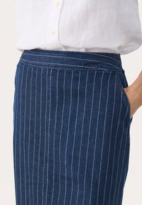 Falda de mezclilla en azul oscuro con rayas verticales blancas. Presenta una cintura alta, bolsillos laterales y una textura suave.