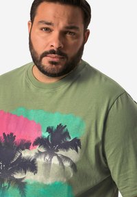 Zelené bavlněné tričko s krátkými rukávy. Obsahuje grafický potisk černých palm na pozadí růžové a tyrkysové akvarelu.