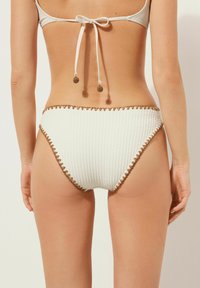 Hochgeschnittene weiße Bikinihose aus Strukturstoff, mit brauner gewellter Zierleiste und hinten gebundenen Bändern mit dekorativen Perlen.