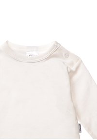 Cremfarbener Langarmtop aus weichem Baumwollstoff, mit Schulterknöpfen und rundem Halsausschnitt. Glatte Textur mit minimaler Detailgestaltung.