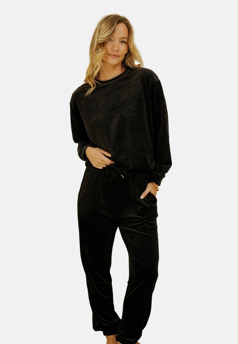 Ensemble de loungewear en velours noir comprenant un haut à manches longues et un pantalon avec une taille élastiquée et des poches. Texture douce et coupe décontractée.