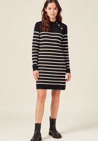 Abito a maniche lunghe in maglia con righe orizzontali nere e crema, scollatura rotonda e tre bottoni decorativi sulla spalla.
