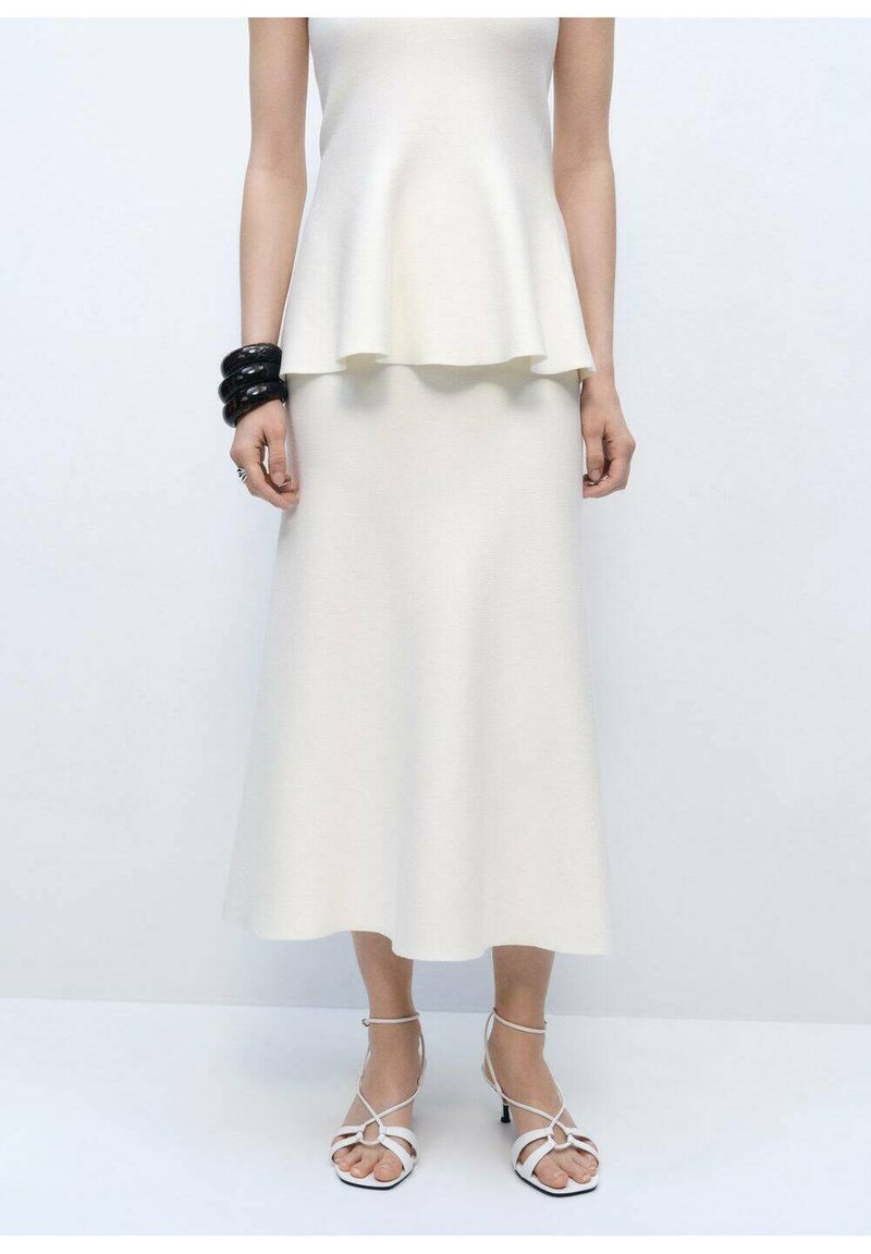 Bílý peplum top spárovaný s volnou midi sukní. Texturovaná látka, kulaté černé náramky na zápěstí a bílé sandály na páscích.