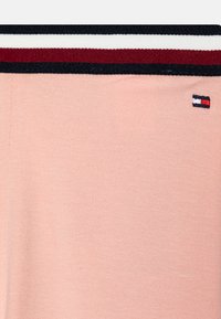 Pinker Baumwollstoff mit einem gestrickten Bund in Marineblau, Weiß und Bordeauxrot sowie einem kleinen gestickten Logo an der Seite.