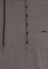 Tissu gris texturé avec deux cordons noirs, l'un affichant en répétition le texte blanc "MICHAEL KORS", et un petit logo "MK" noir brodé.