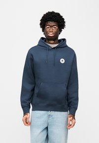 Μπλε ναυτικό φούτερ με κουκούλα κατασκευασμένο από βαμβακερό μείγμα, με μπροστινή τσέπη και κυκλικό λογότυπο με αστέρι στο αριστερό στήθος. Απλός σχεδιασμός.