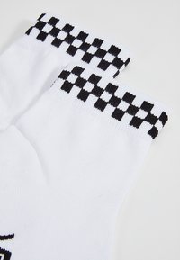 Weiße Socken mit einem schwarzen karierten Muster am Bund, aus weichem Stoff mit geripptem Textur, entworfen für Komfort und Passform.