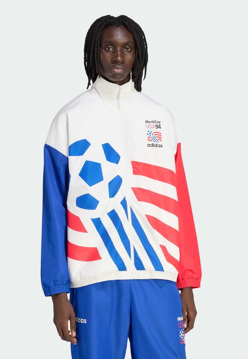 Άτομο που φοράει μπουφάν Adidas USA 1994 World Cup και μπλε παντελόνι με γραφικό σχέδιο ποδοσφαίρου σε κόκκινο, άσπρο και μπλε.