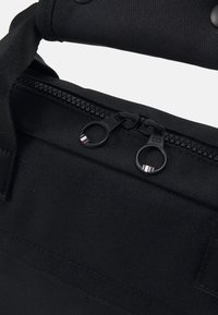 Zwarte stoffen tas met een ritsopening, voorzien van twee zwarte ritsen met metalen accenten en een stevige handgreep aan de bovenkant.