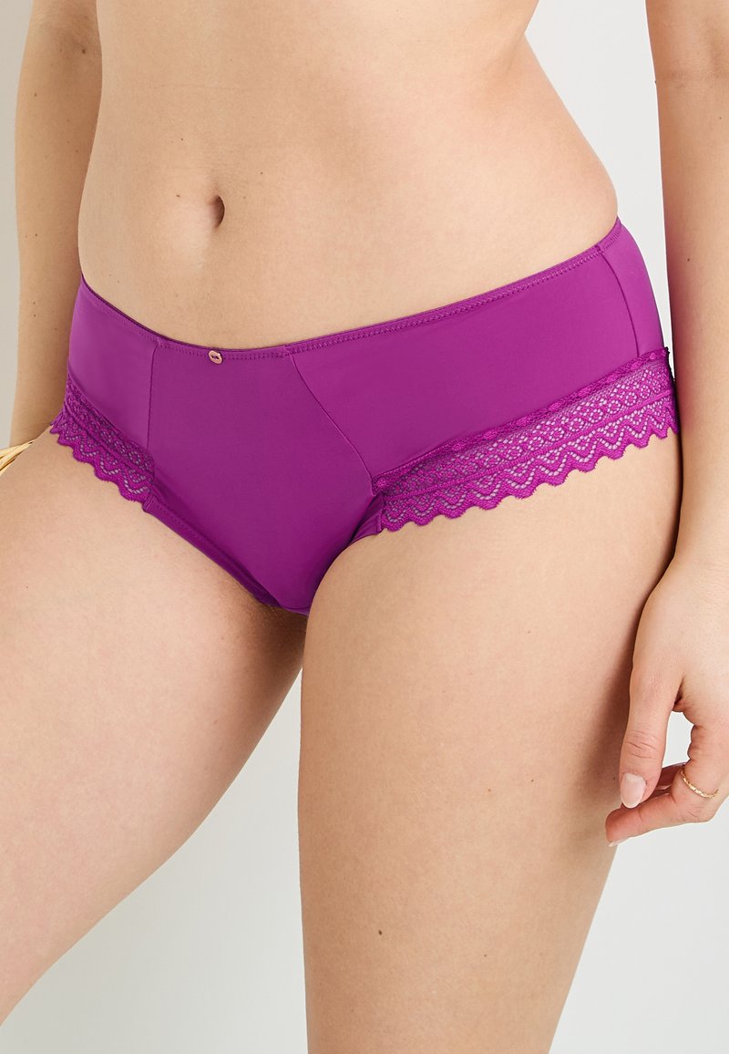 Pantaloni corti viola realizzati in un materiale morbido e elastico, con pizzo lungo i bordi. Il design include un motivo a scollatura.