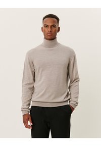 Hellbeige Rollkragenpullover aus weichem Strickstoff, mit langen Ärmeln und geripptem Saum, sowie einem dezenten Logodetail auf der Brust.